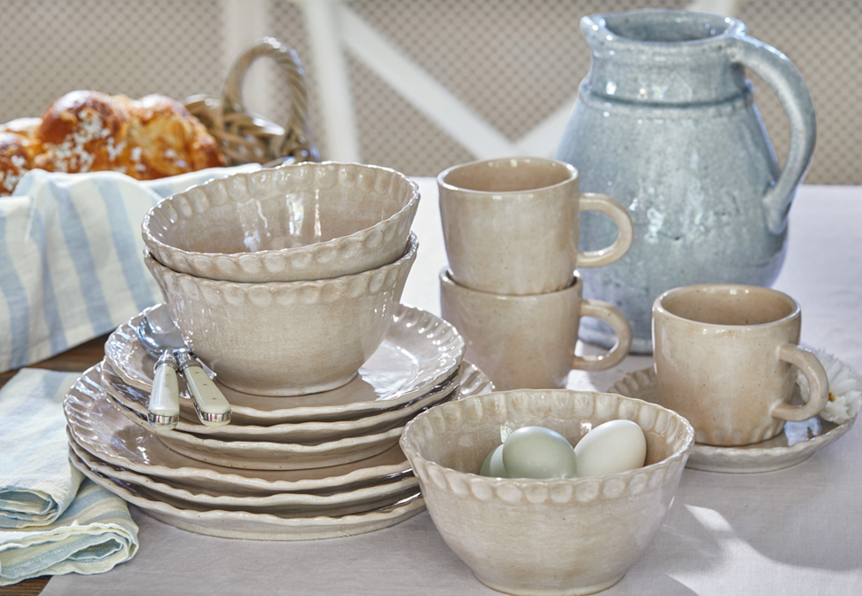 Beige keramiek servies met borden, kommen en mokken op rustieke tafel