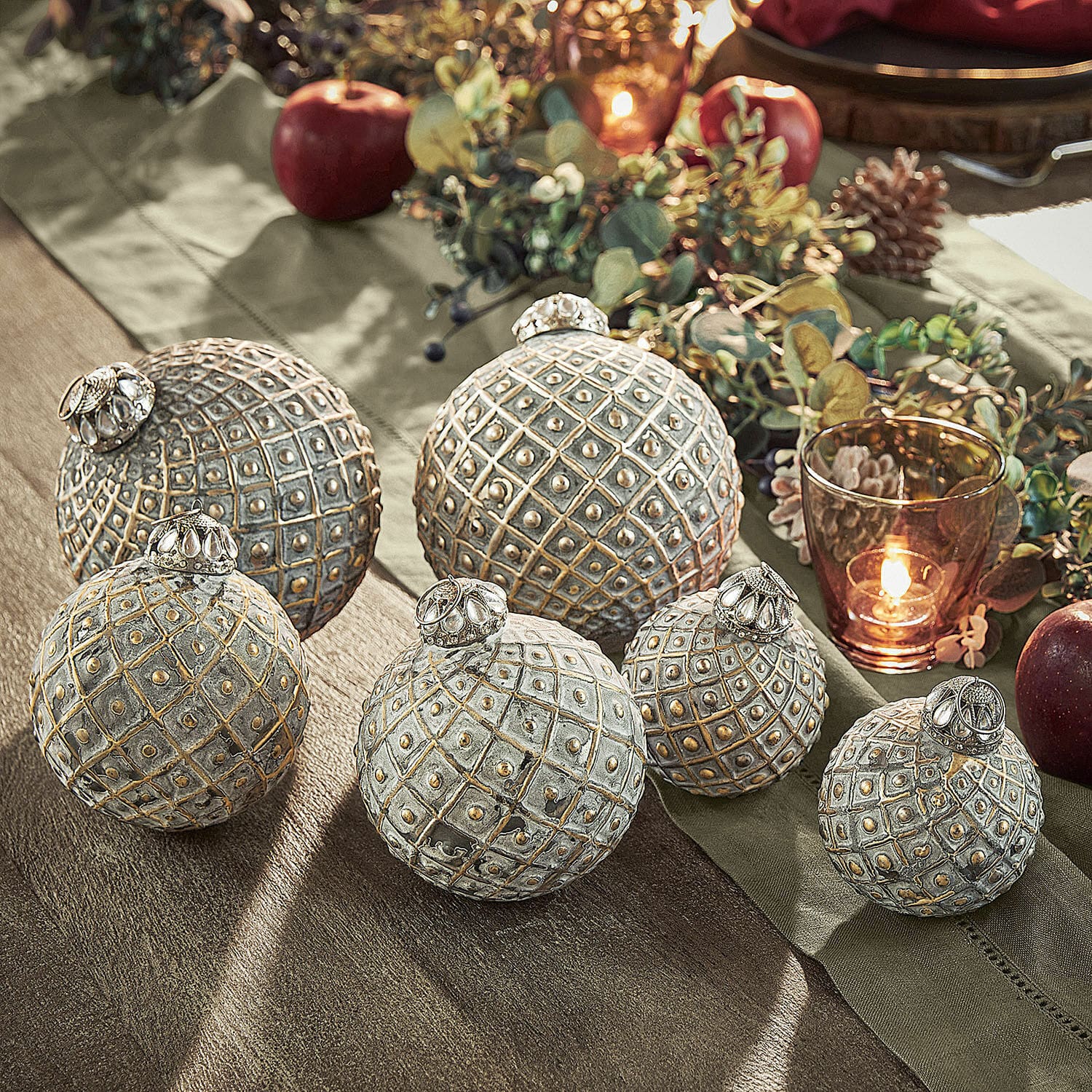 Kerstversiering set van 6 Lucero Set van zes decoratieve metalen ballen in grijs-gouden kleur op feestelijke tafel met appels en kaars