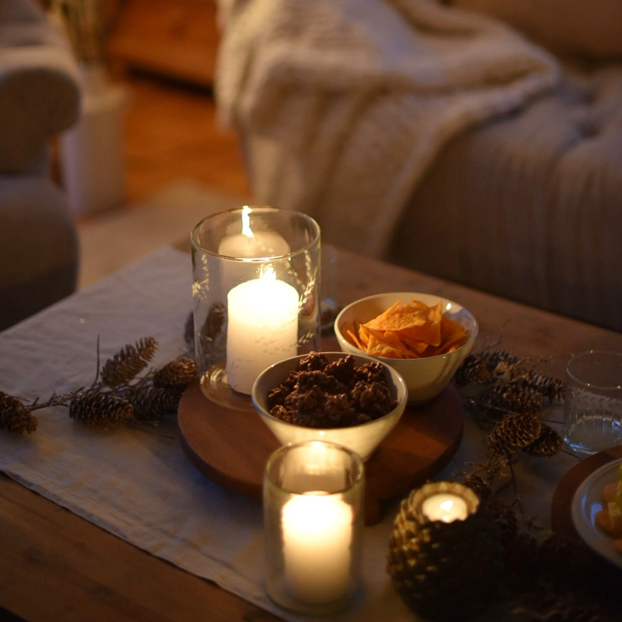 Kaarsen in glazen houders en schaaltjes met snacks op houten tafel in een gezellige kamer