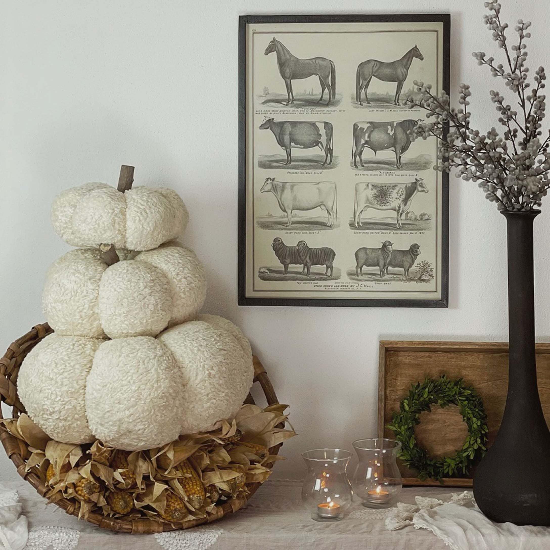 Herfstdecoratie met witte pluchen pompoen in rieten mand en kaarsen op tafel