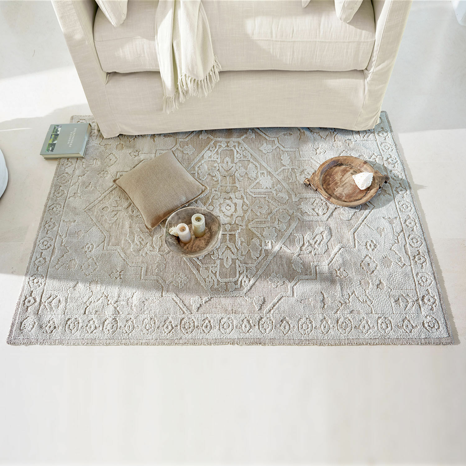 Beige tapijt met patroon onder lichte bank met kussen en houten decoraties in lichte woonkamer