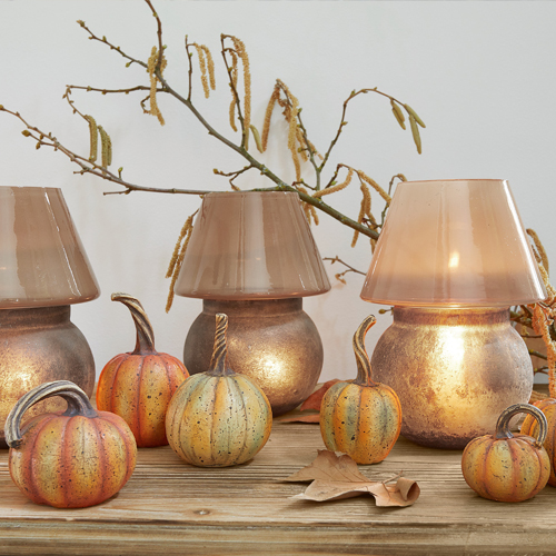 Decoratieve lantaarns van koperkleurig glas en metaal met pompoendecoraties op houten tafel