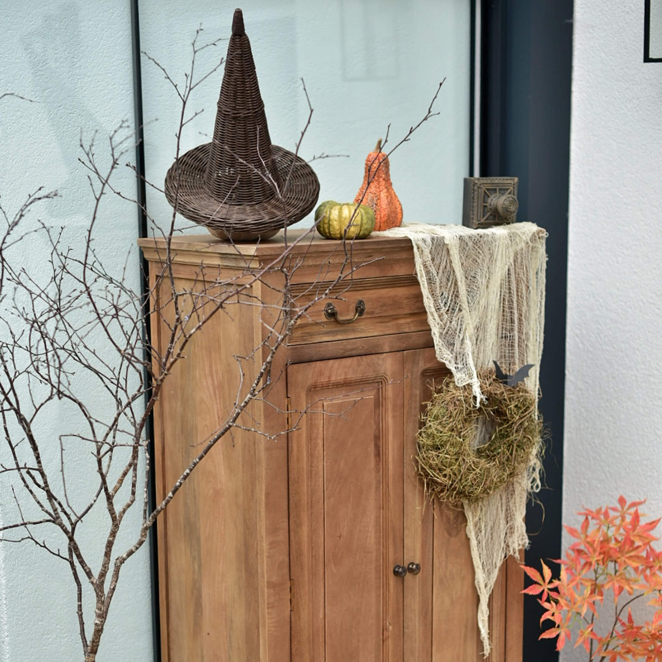 Houten kast met herfstdecoratie: gevlochten hoed, pompoenen en moskrans