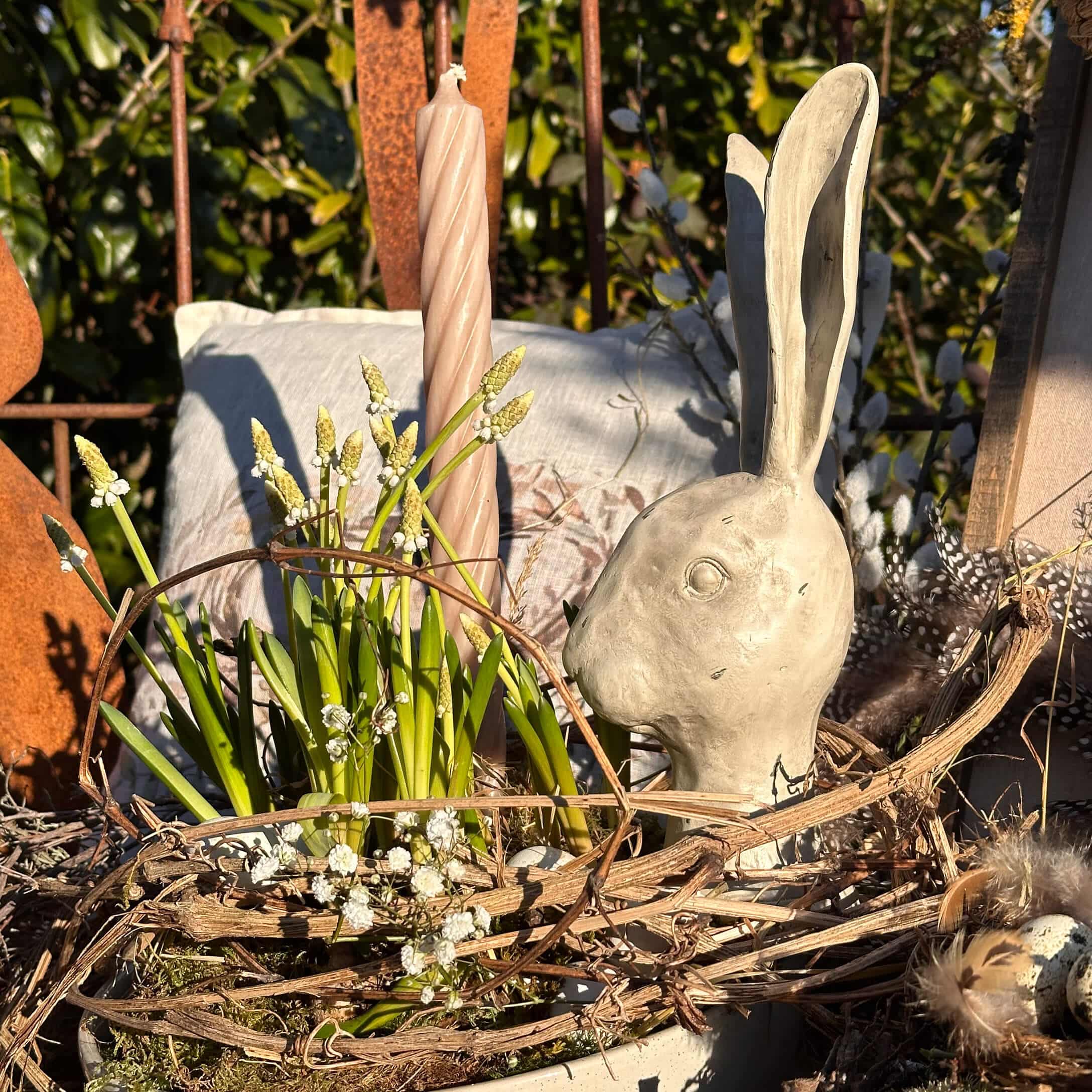 Natuurlijke paasdecoratie met grijs keramisch konijnenhoofd en groene bloemen in een natuurlijke mand