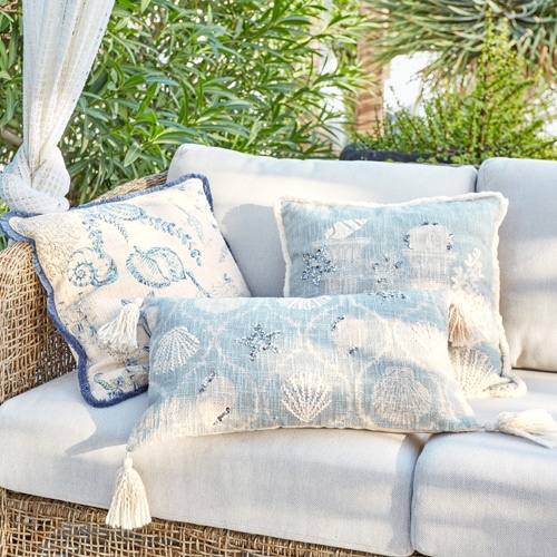 Decoratieve kussens met schelpenmotief op lichte rotanbank in tuin