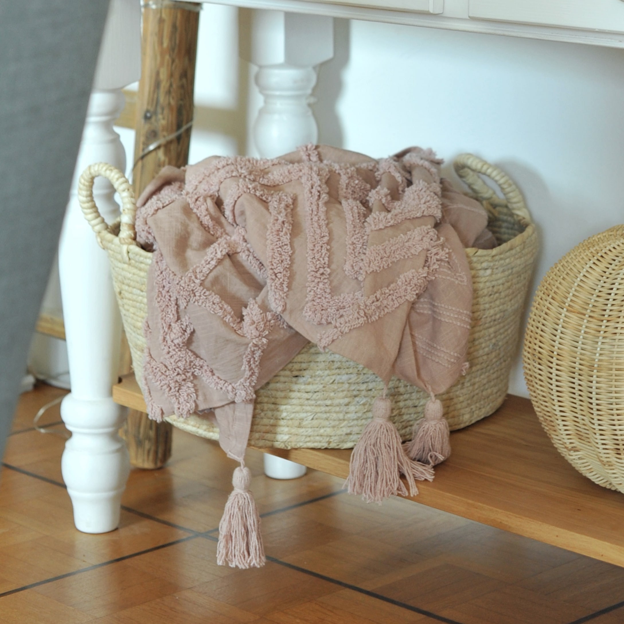 Roze decoratief deken met franjes van zacht materiaal in een rieten mand op een houten plank