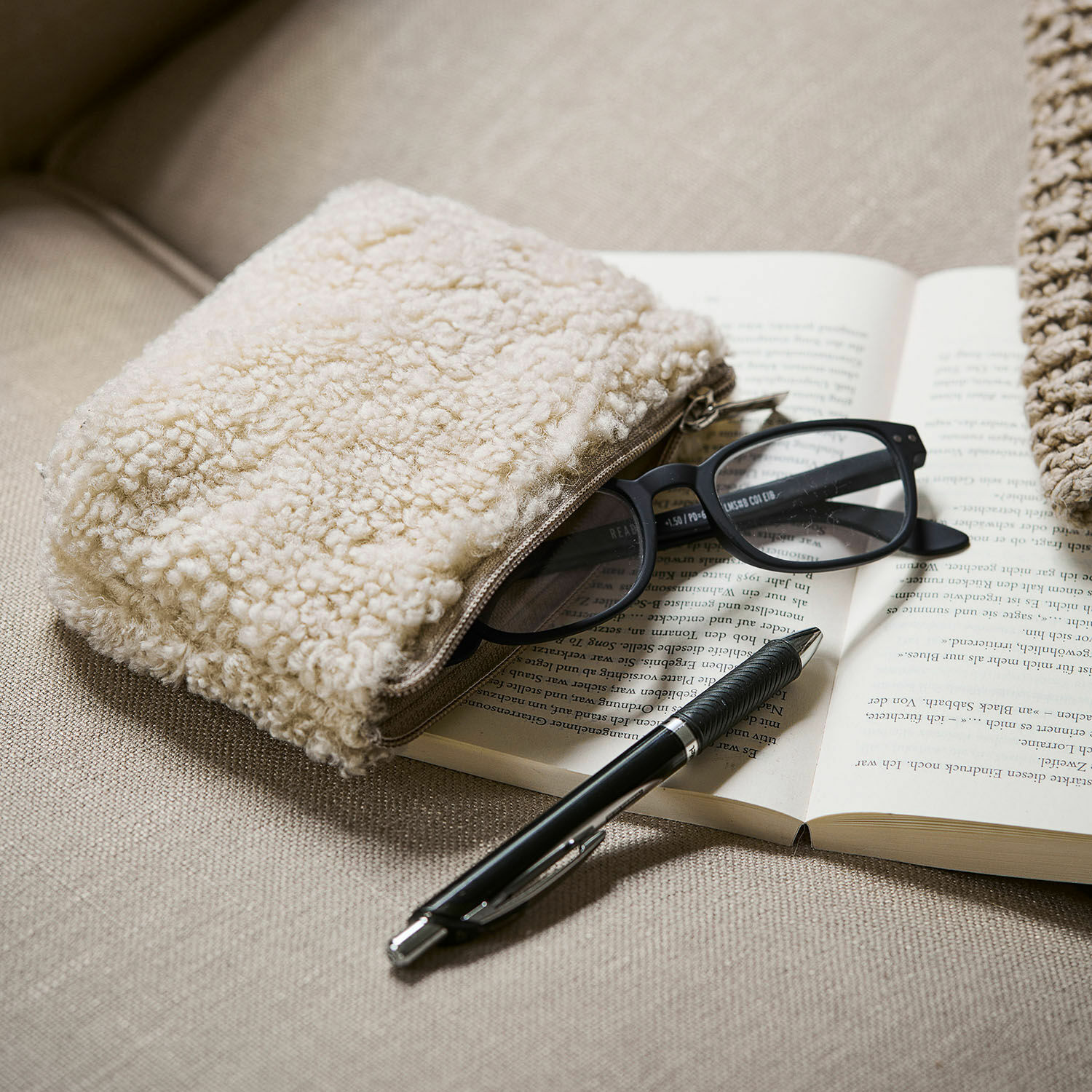 Tasje Bathilde Beige zachte make-uptas van schapenvachtmateriaal op bank met bril en zwarte pen