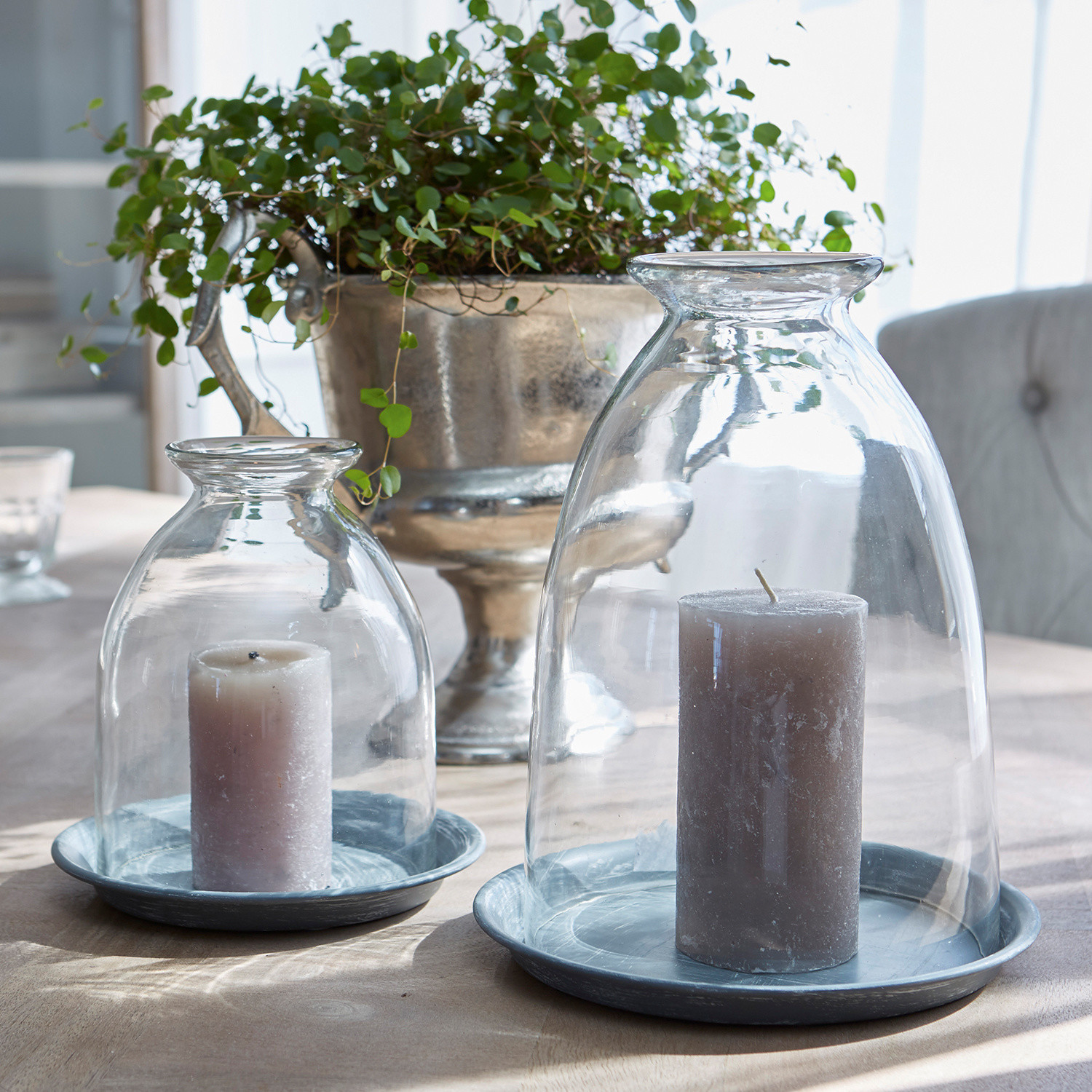 Windlicht set van 2 Gwendale Grijze kaarsen onder transparante glazen stolpen op grijze metalen schalen op een tafel