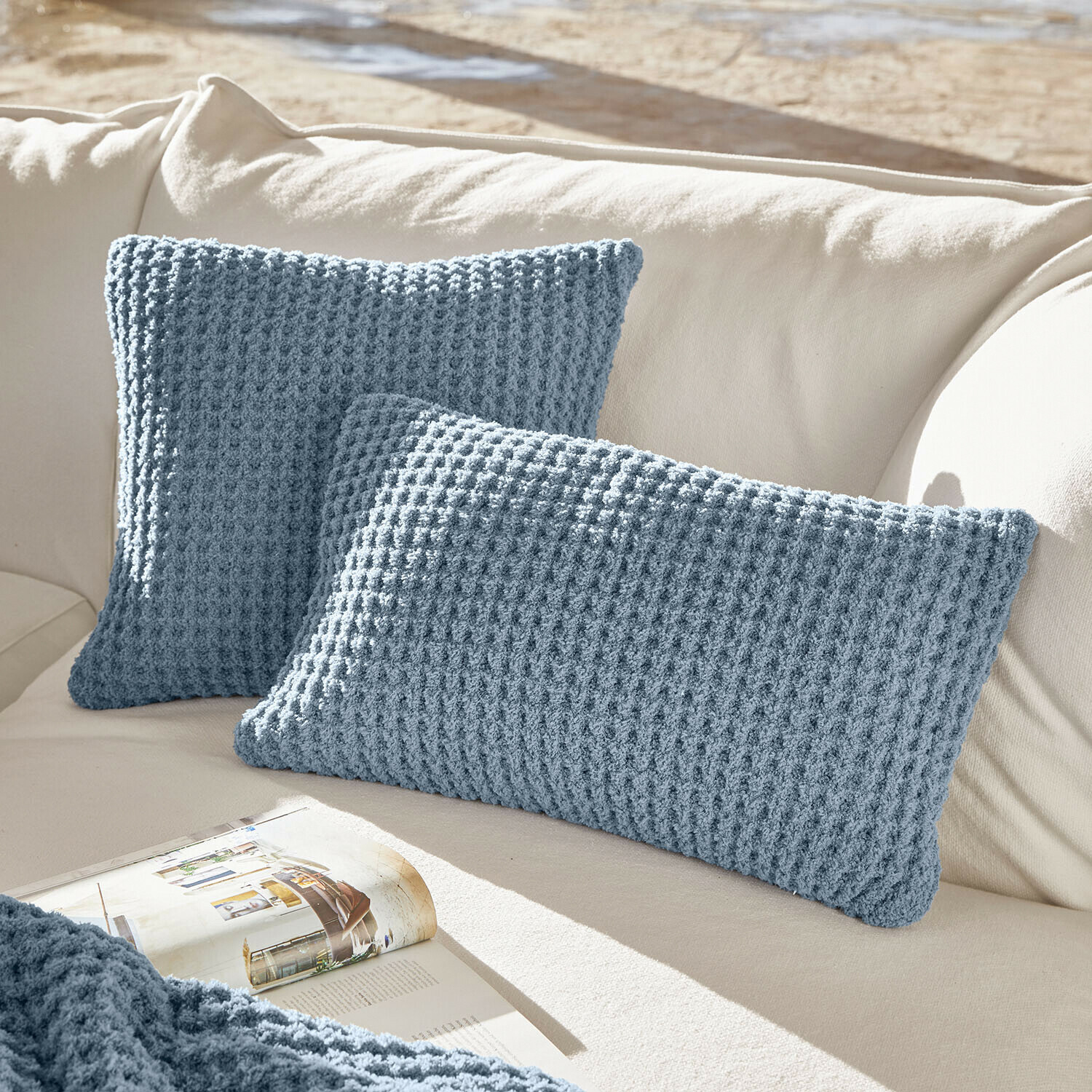 Kussenhoes set van 2 Ysilda Twee blauwe gebreide kussens op crèmekleurige bank, zachte woondecoratie voor woonkamer