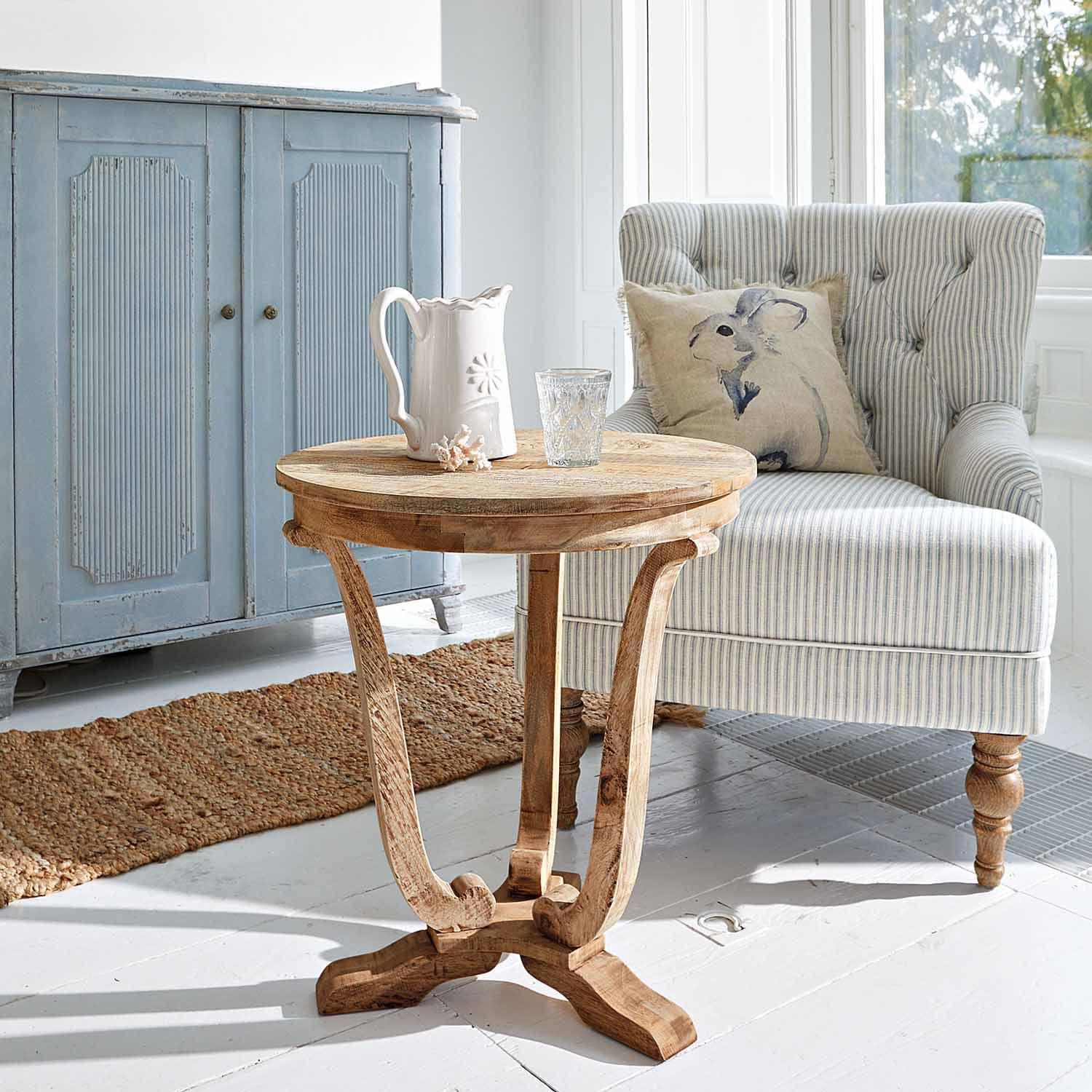Ronde bijzettafel van mangohout in natuurlijke kleur in lichte woonkamer met gestreepte fauteuil en blauwe kast