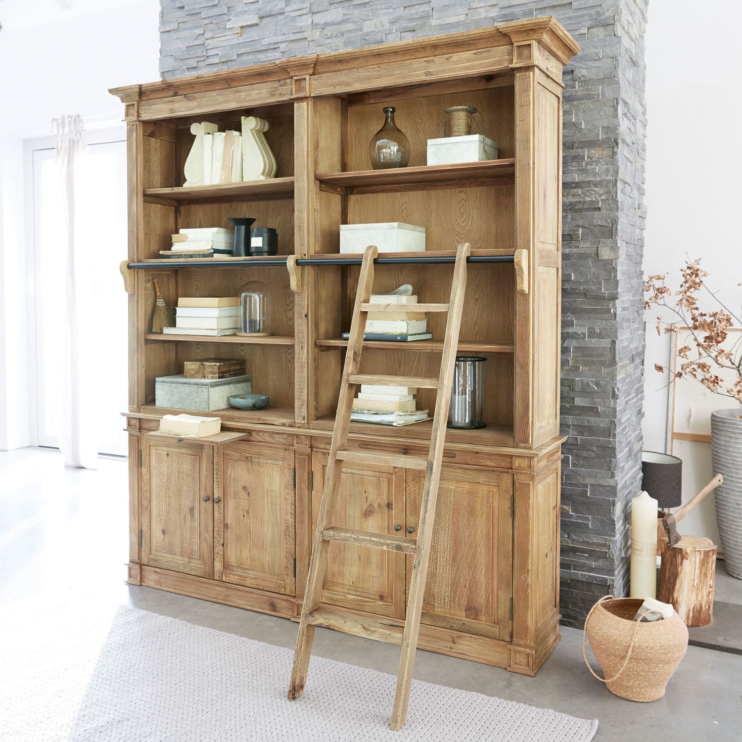 Grote houten boekenkast met ladder en planken vol boeken en decoraties in lichte kamer