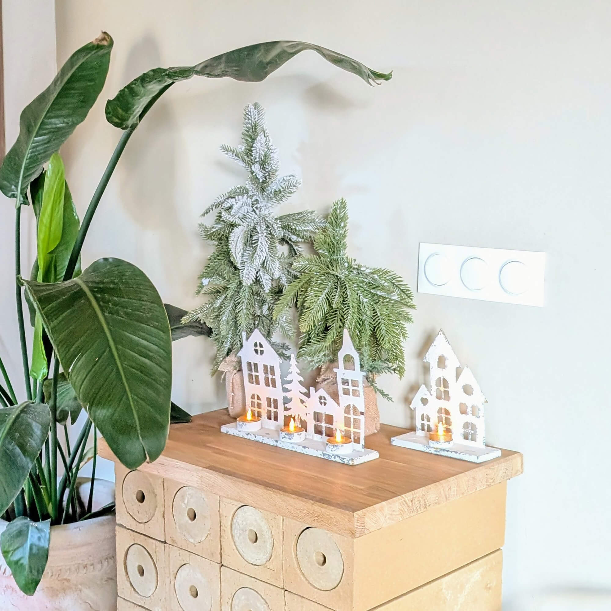 Kerstdecoratie met witte houten huisjes en groene takken op een licht houten blad