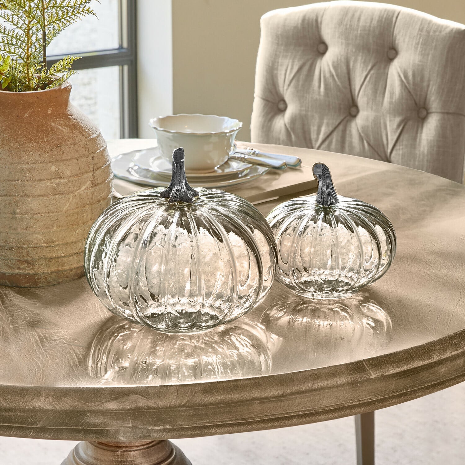 Pompoen set van 2 Perlouin Twee transparante glazen pompoenen met metalen stelen op een beige decoratieve tafel