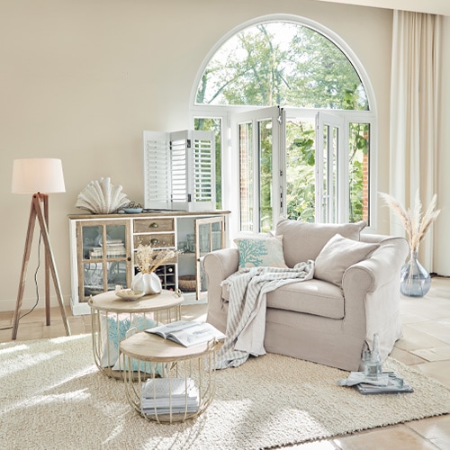 Beige stoffen fauteuil in lichte woonkamer met ronde tafels en houten vloerlamp