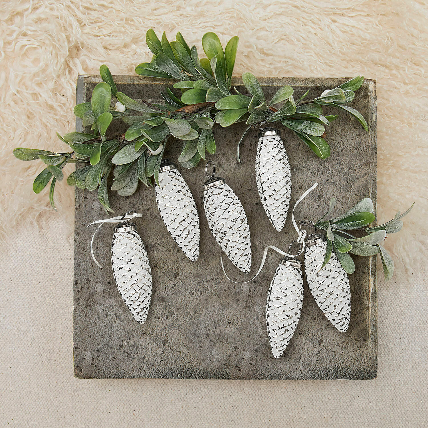 Witte metalen dennenappelversieringen met groene bladeren op grijze achtergrond, kerstdecoratie