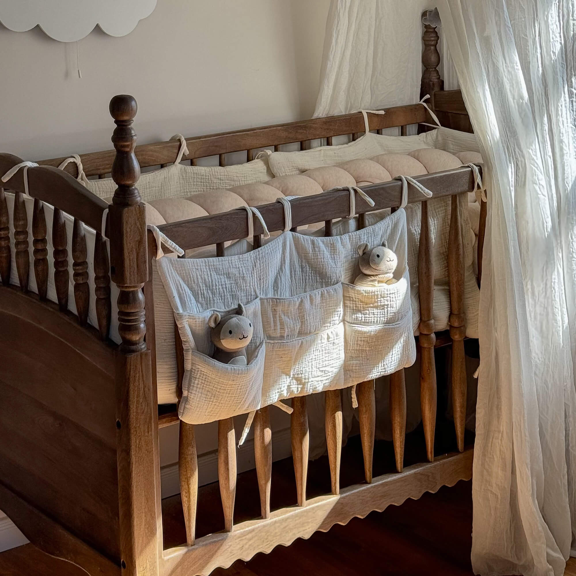 Houten babybed met crèmekleurige katoenen beschermer en knuffels in de zakken voor kinderkamer