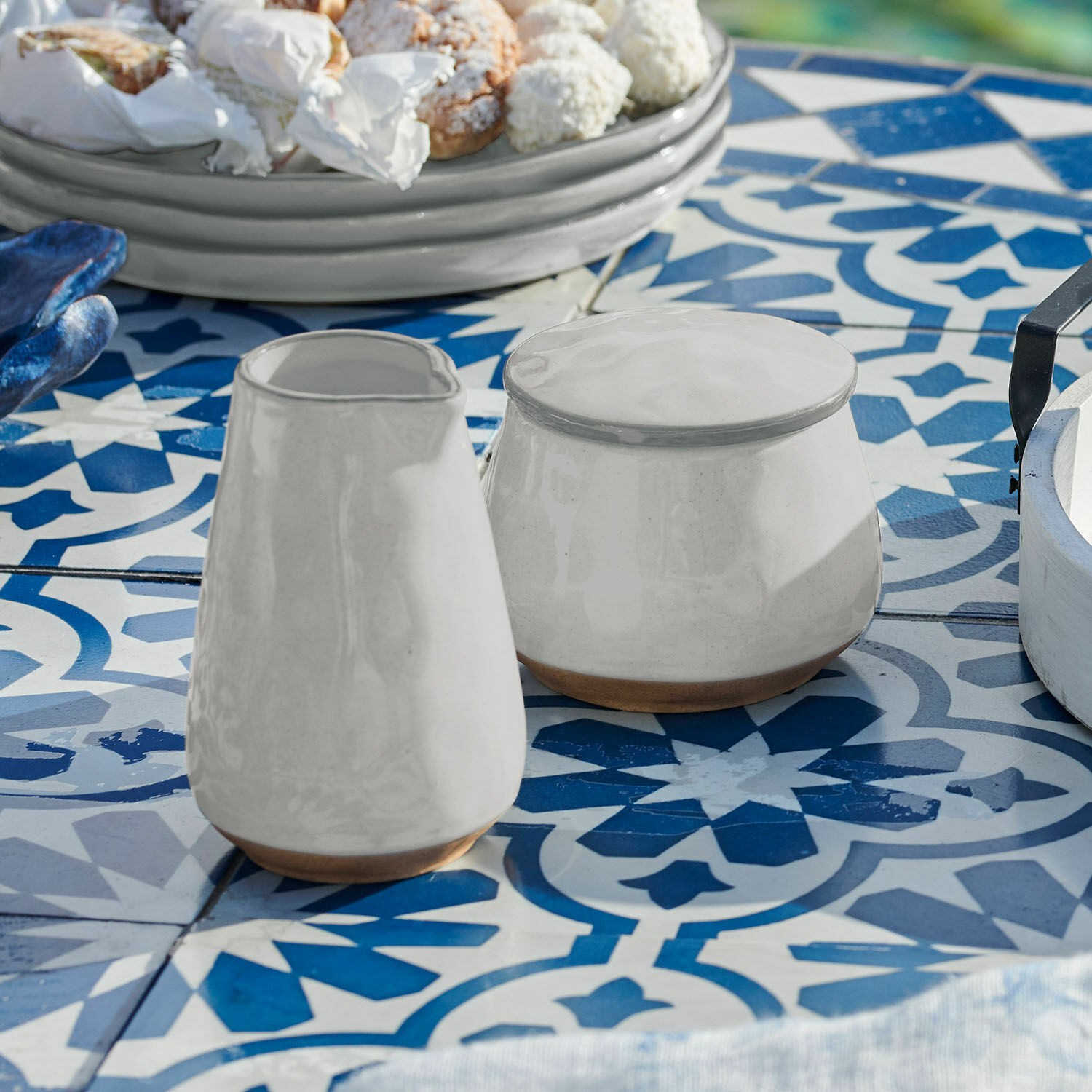 Suikerpotje en melkkannetje Biarré Witte keramische kan en suikerpot met natuurlijke bruine bodem op blauw-witte tegeltafel