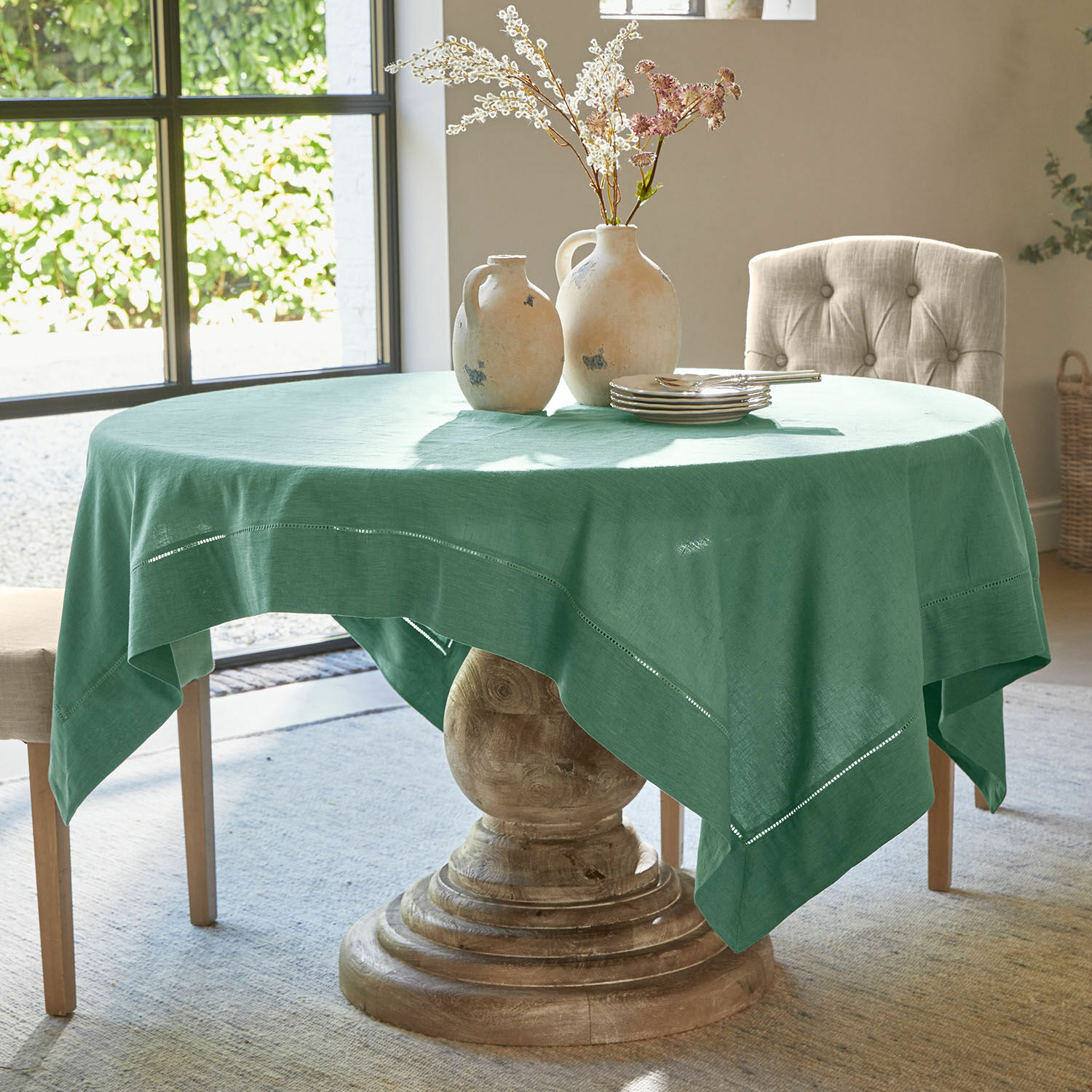 Ronde tafel met houten voet en groene linnen tafelkleed, versierd met keramische vazen en borden