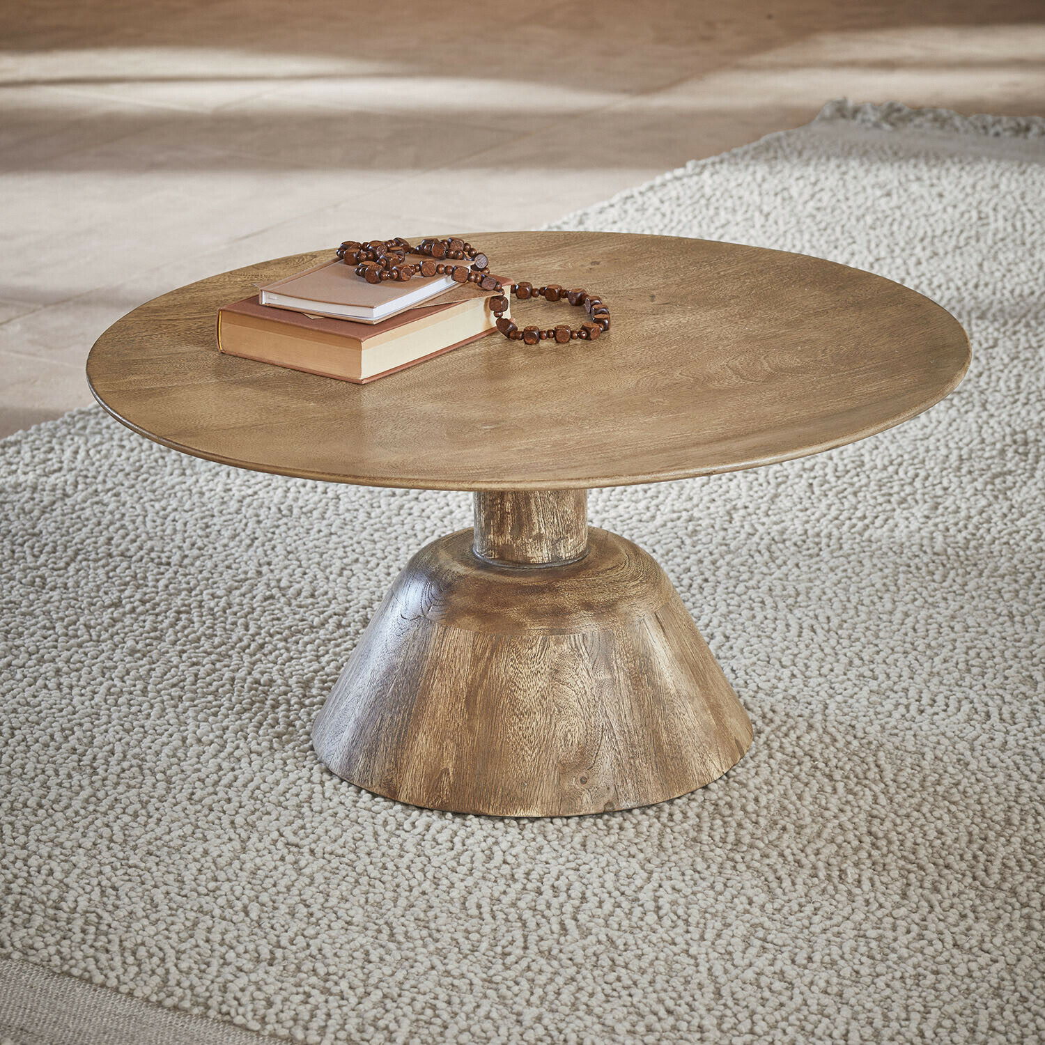 Salontafel Ulric Ronde houten salontafel in natuurlijke kleur op lichte vloerkleed met boeken en kralenketting