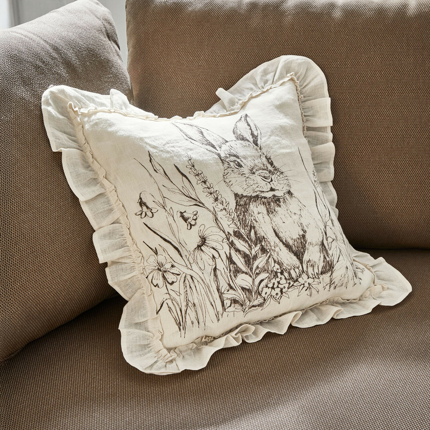 Beige linnen kussen met ruches en konijn met bloemenprint op bruine bank