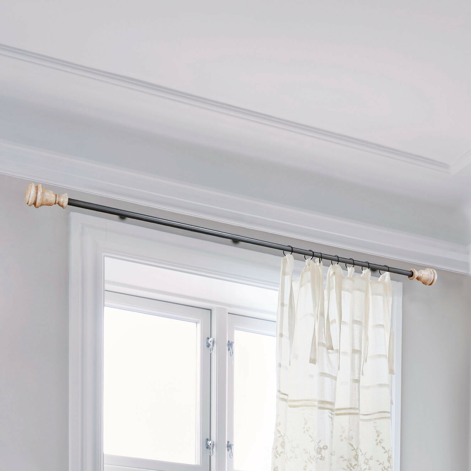 Zwarte metalen gordijnroede met lichte houten uiteinden en witte geborduurde gordijnstof