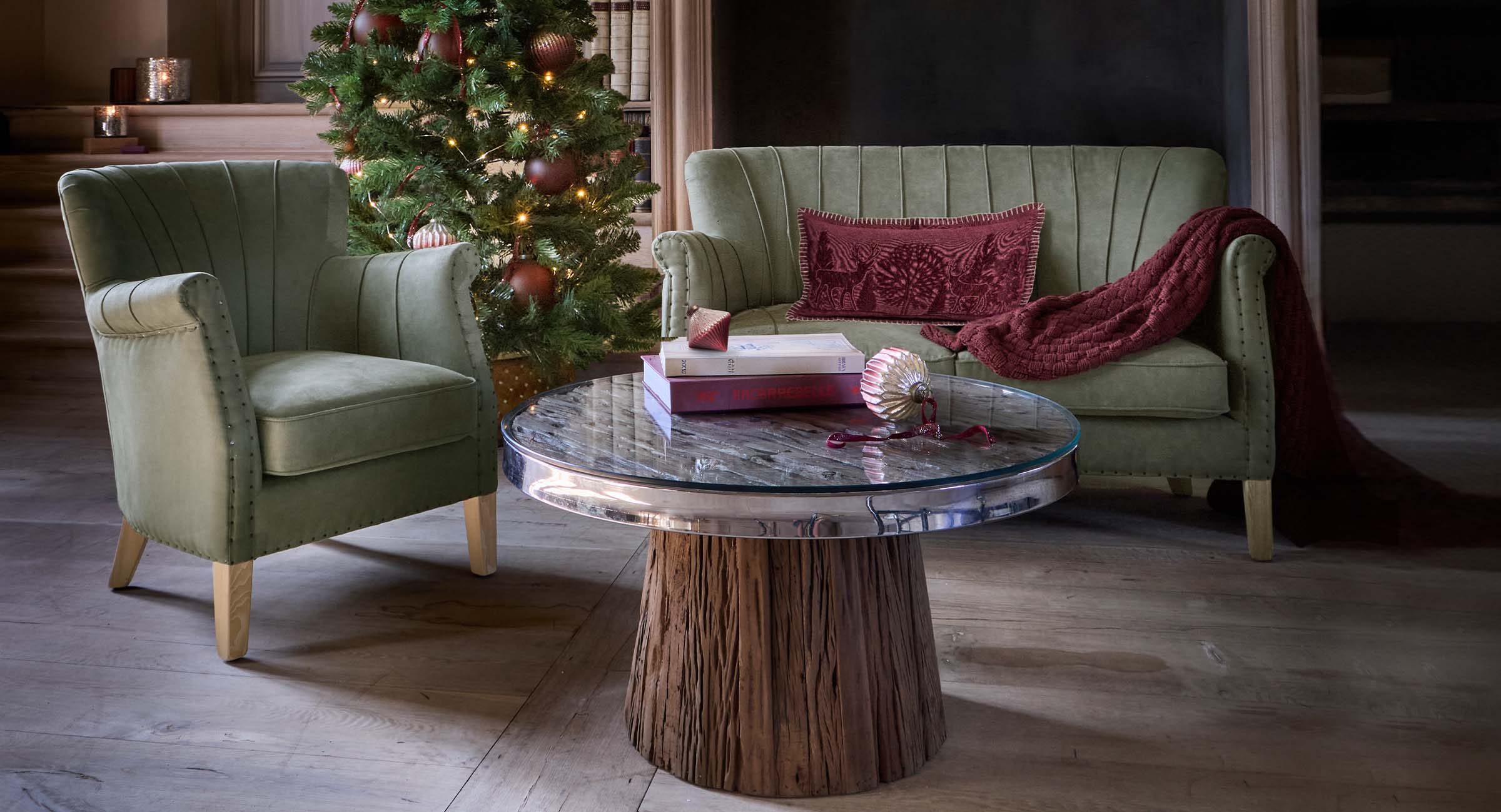 Groene fluwelen fauteuil en bank met rood kussen en deken bij kerstboom in rustieke woonkamer