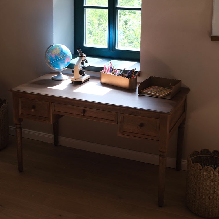 Houten bureau met drie lades bij het raam, globe en microscoop op het blad