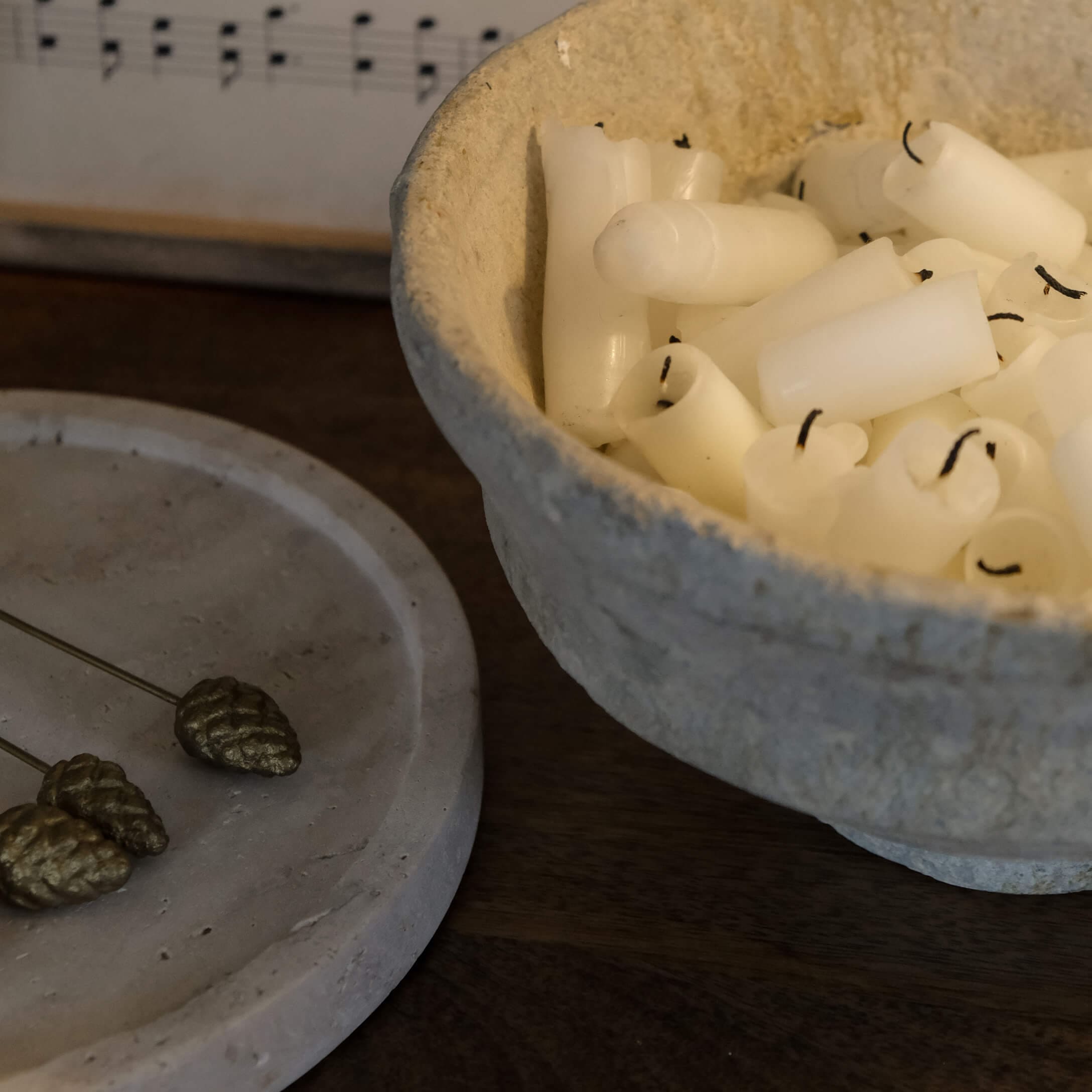 Kom van natuurlijk materiaal gevuld met witte kaarsen op een donkere houten tafel, sfeervolle decoratie
