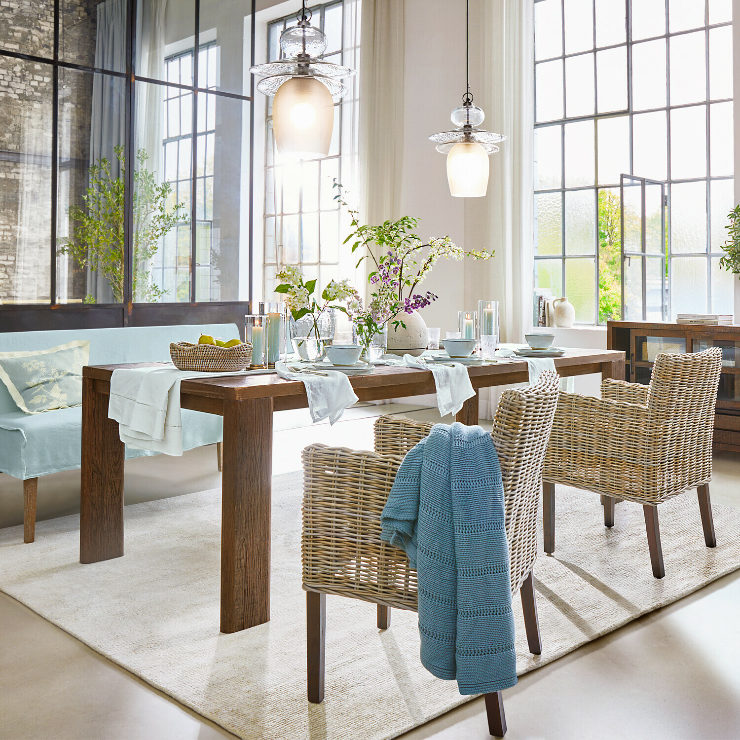 Eetkamer met houten tafel, rotan stoelen en rustieke decoratieve verlichting