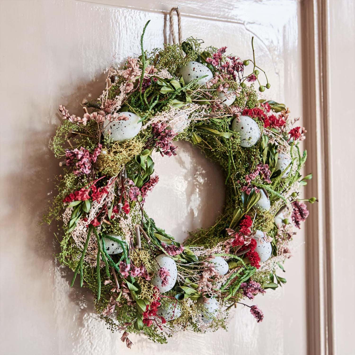 Decoratieve krans van groene takken, roze bloemen en blauwe nep-eieren aan de deur