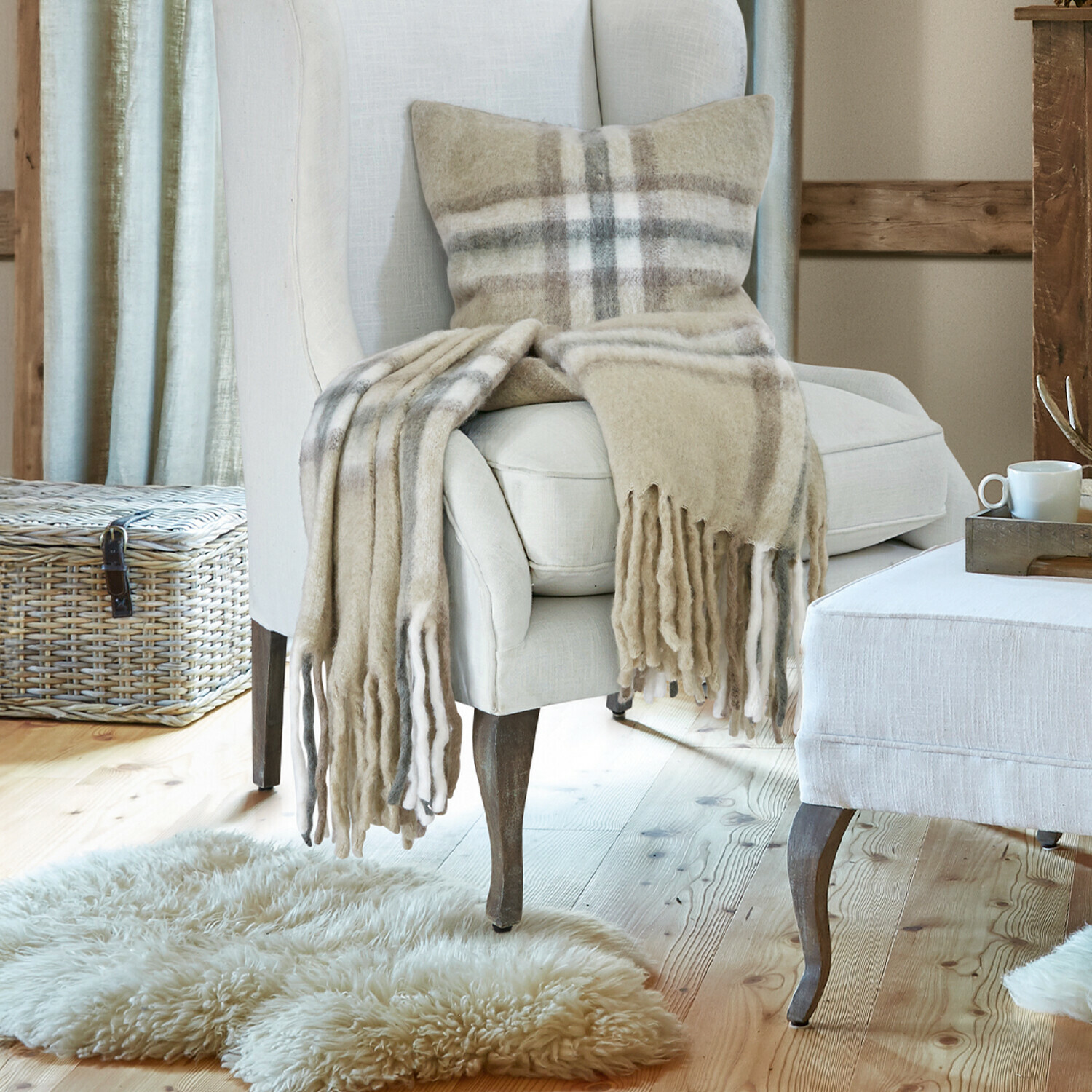 Plaid Klinas Beige stoffen fauteuil en voetenbank in gezellige woonkamer met houten vloer en open haard