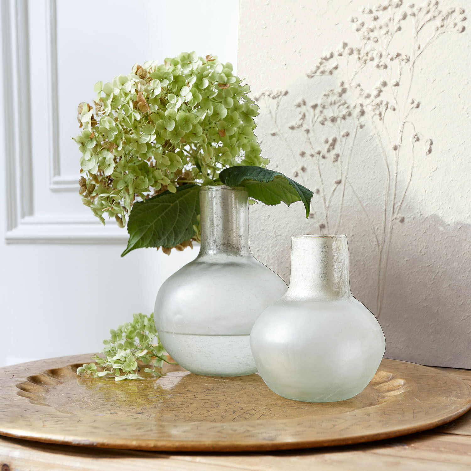 Vaas set van 2 Nazira Twee matte melkglas vazen op een gouden dienblad met groene hortensia bloemen