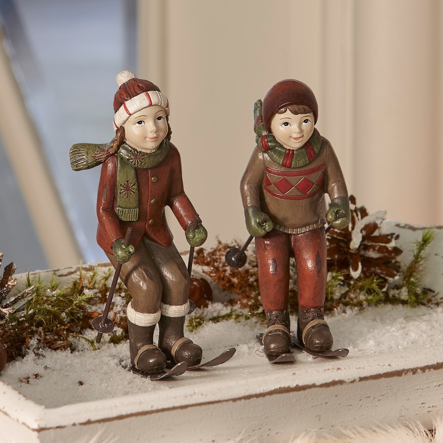 Figuurtje set van 2 Bibury Beeldjes van kinderen in bruin-rode kleding op ski's als winterse kerstdecoratie