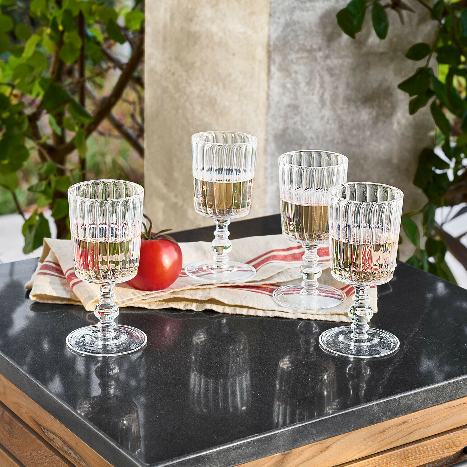 Vier transparante geribbelde glazen met lichte drank op een zwarte stenen tafel