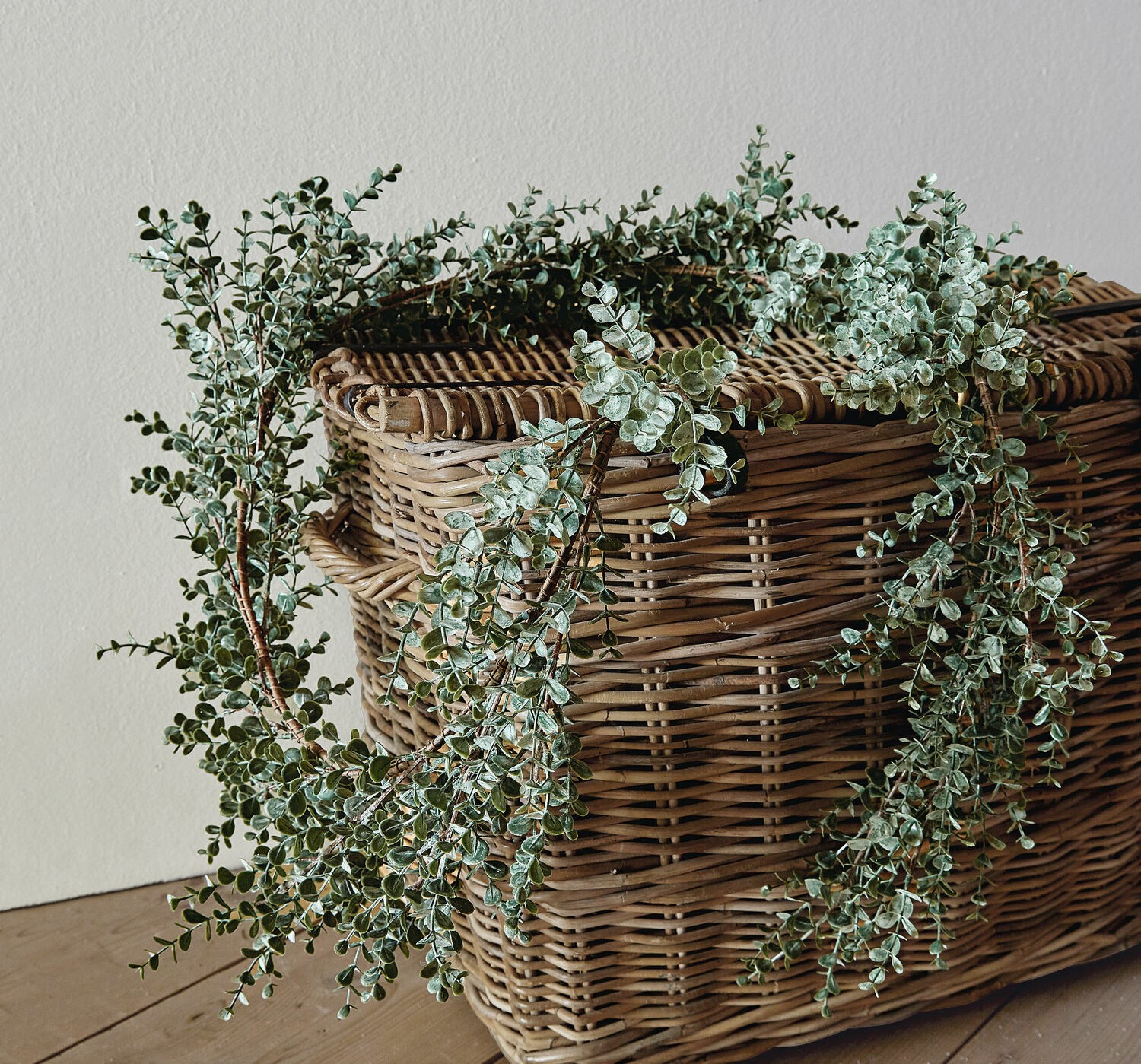Decoratieve krans van groene eucalyptusbladeren op een rieten mand op een houten vloer