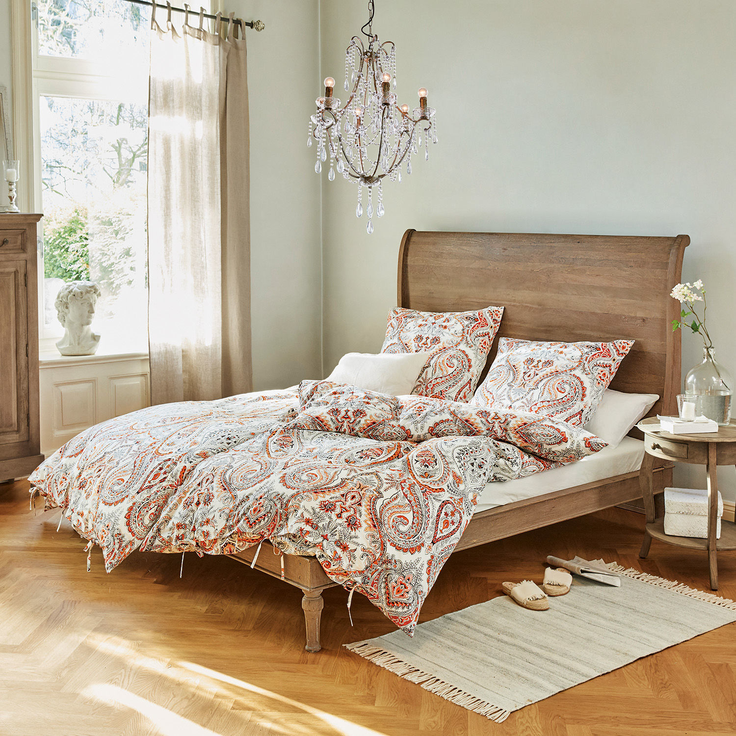Bed Saint-Germier Slaapkamer met houten bed en rood-wit paisley beddengoed, vloerkleed en kristallen kroonluchter
