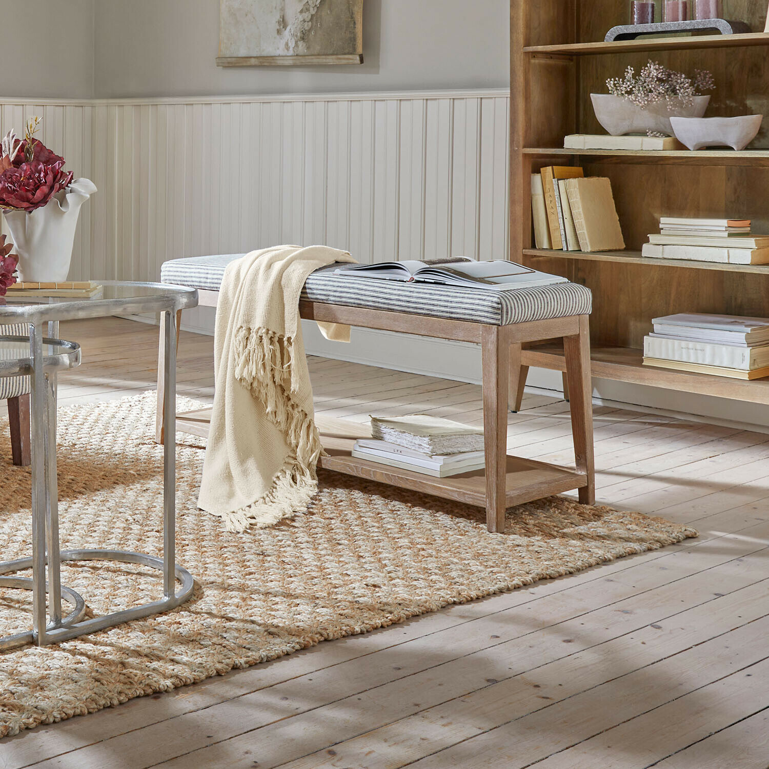 Houten bankje met gestreept gestoffeerd zitvlak en crème deken op natuurlijke vloerkleed in lichte kamer