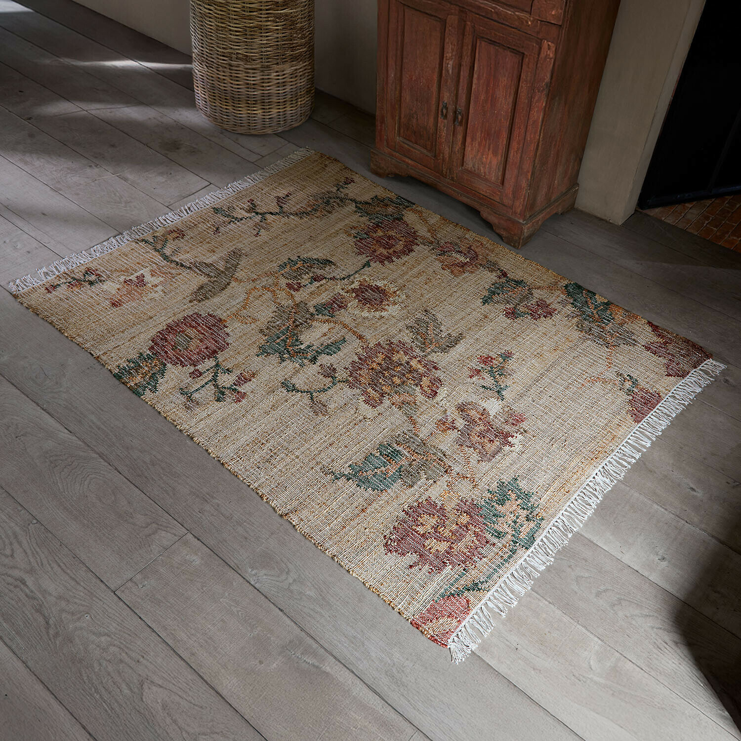 Vloerkleed Caléndoro Beige vloerkleed van natuurlijk materiaal met bloemenpatroon en franjes op lichte houten vloer