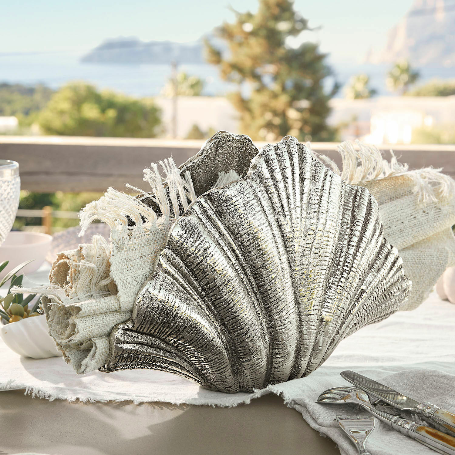 Zilverkleurige metalen schelpdecoratie met natuurlijke linnen servetten op tafel met zeezicht