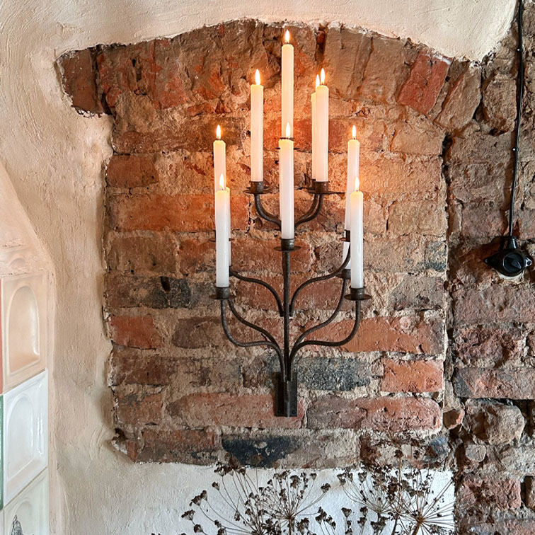 Metalen wandkandelaar met zeven brandende witte kaarsen tegen een bakstenen muur, interieurdecoratie
