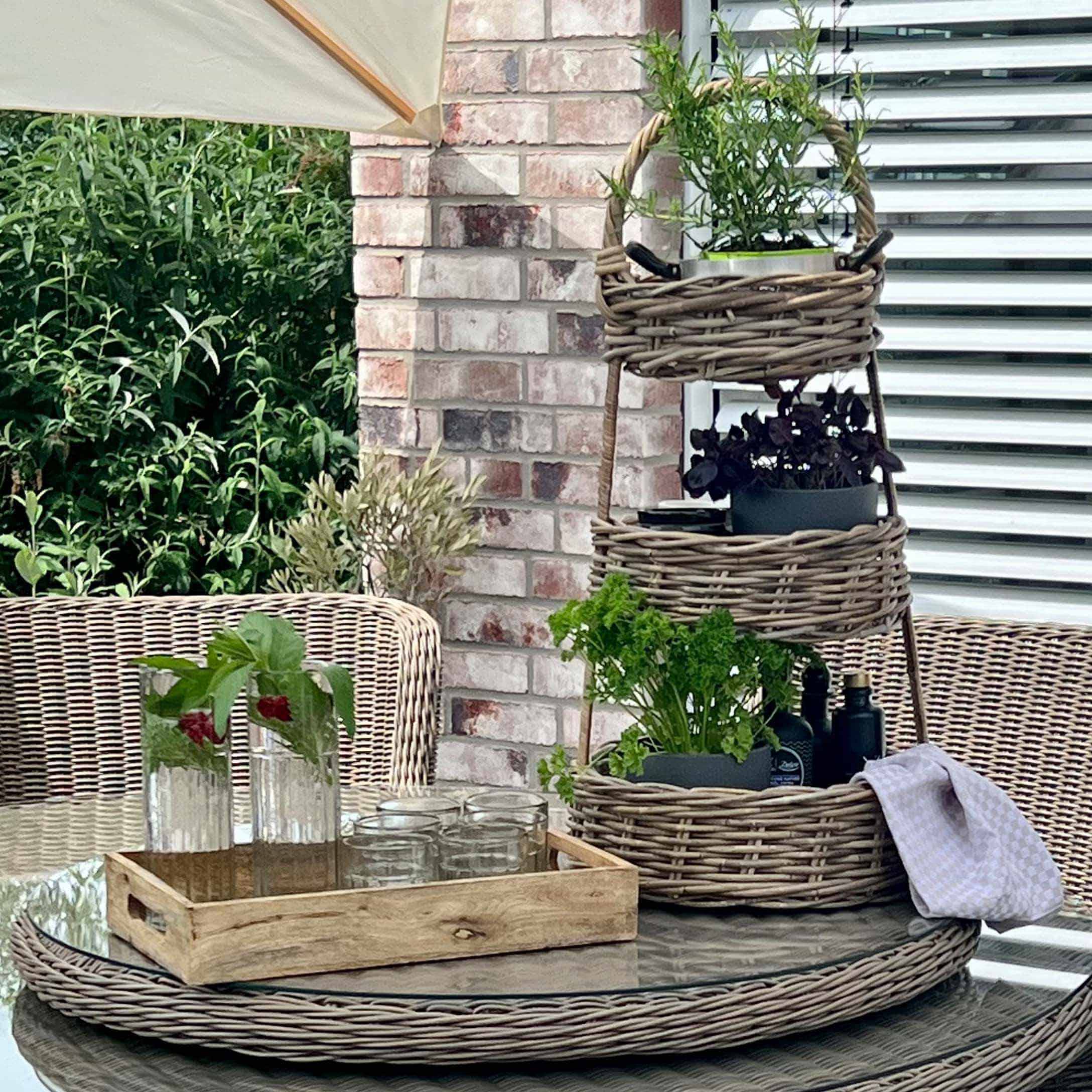 Drie verdiepingen hoge rotan standaard met groene planten op glazen tafel op terras met rotan meubels