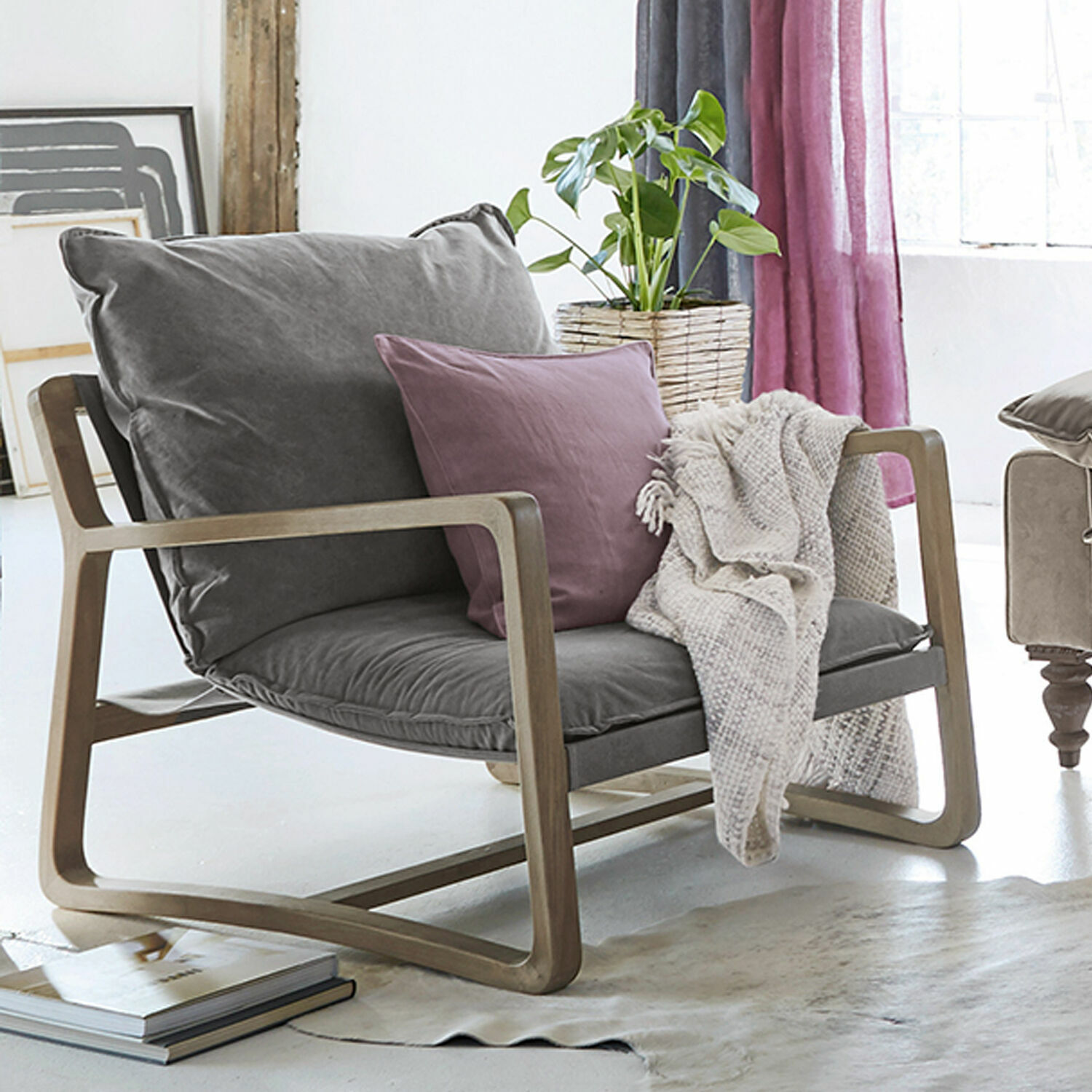 Fauteuil met grijze stof en houten frame, paarse kussen en beige deken in lichte kamer