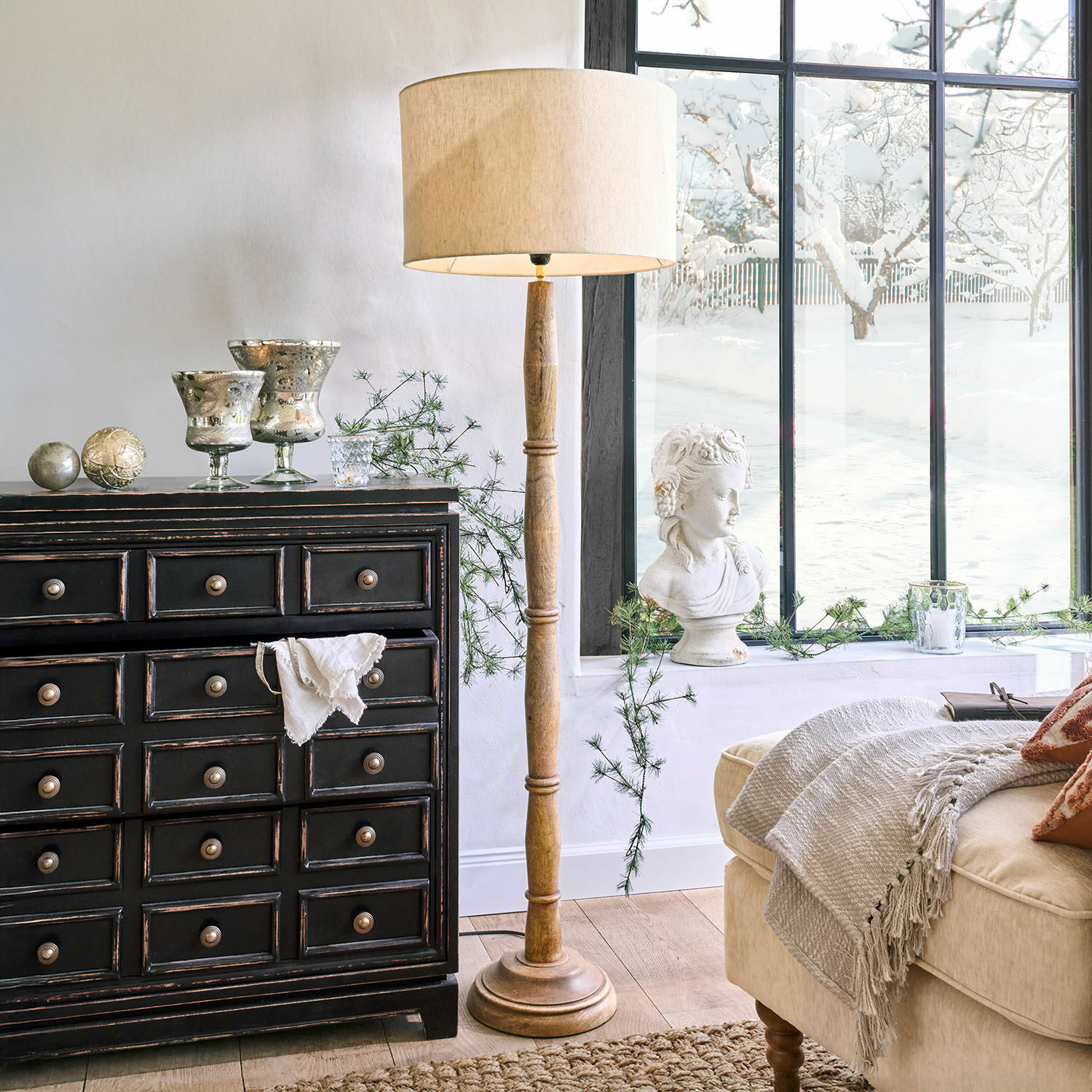 Houten vloerlamp met beige kap in klassieke woonkamer met zwarte ladekast en decoraties