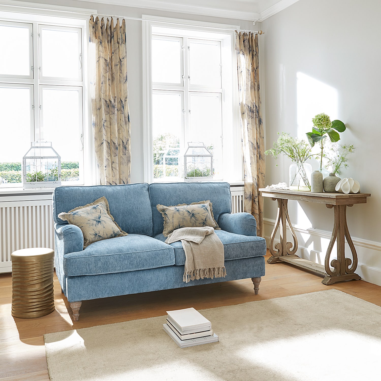 Blauwe gestoffeerde bank met beige kussens en houten tafel in lichte woonkamer