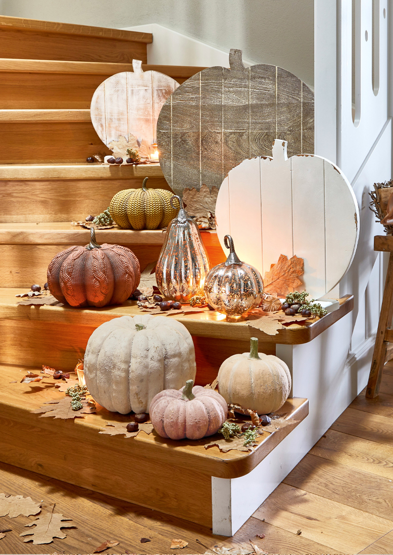 Herfstdecoratie met houten en stoffen pompoenen in pasteltinten op houten trap met herfstbladeren