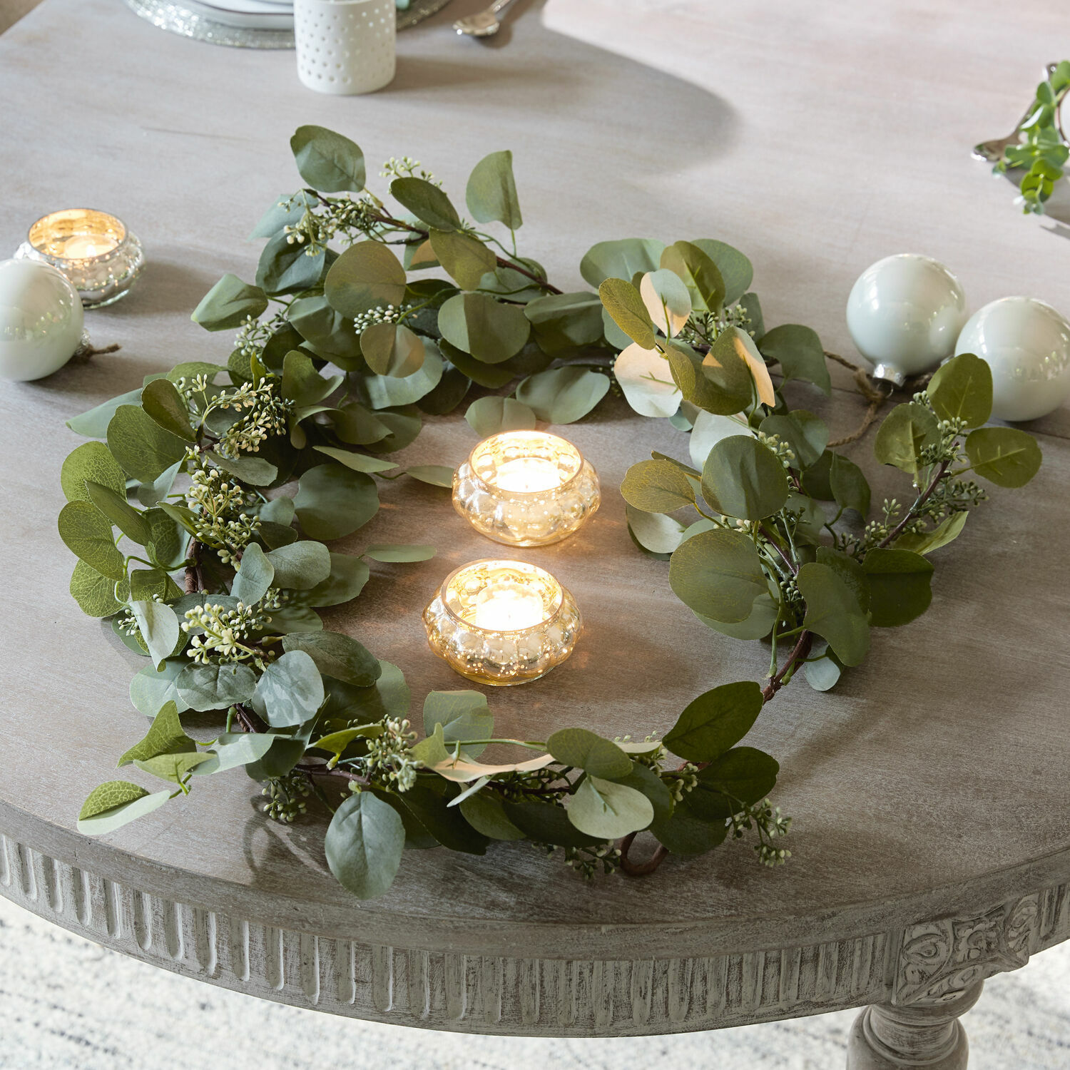 Guirlande Xantos Decoratieve krans van groene bladeren op een grijze tafel met twee kaarsen in glazen houders