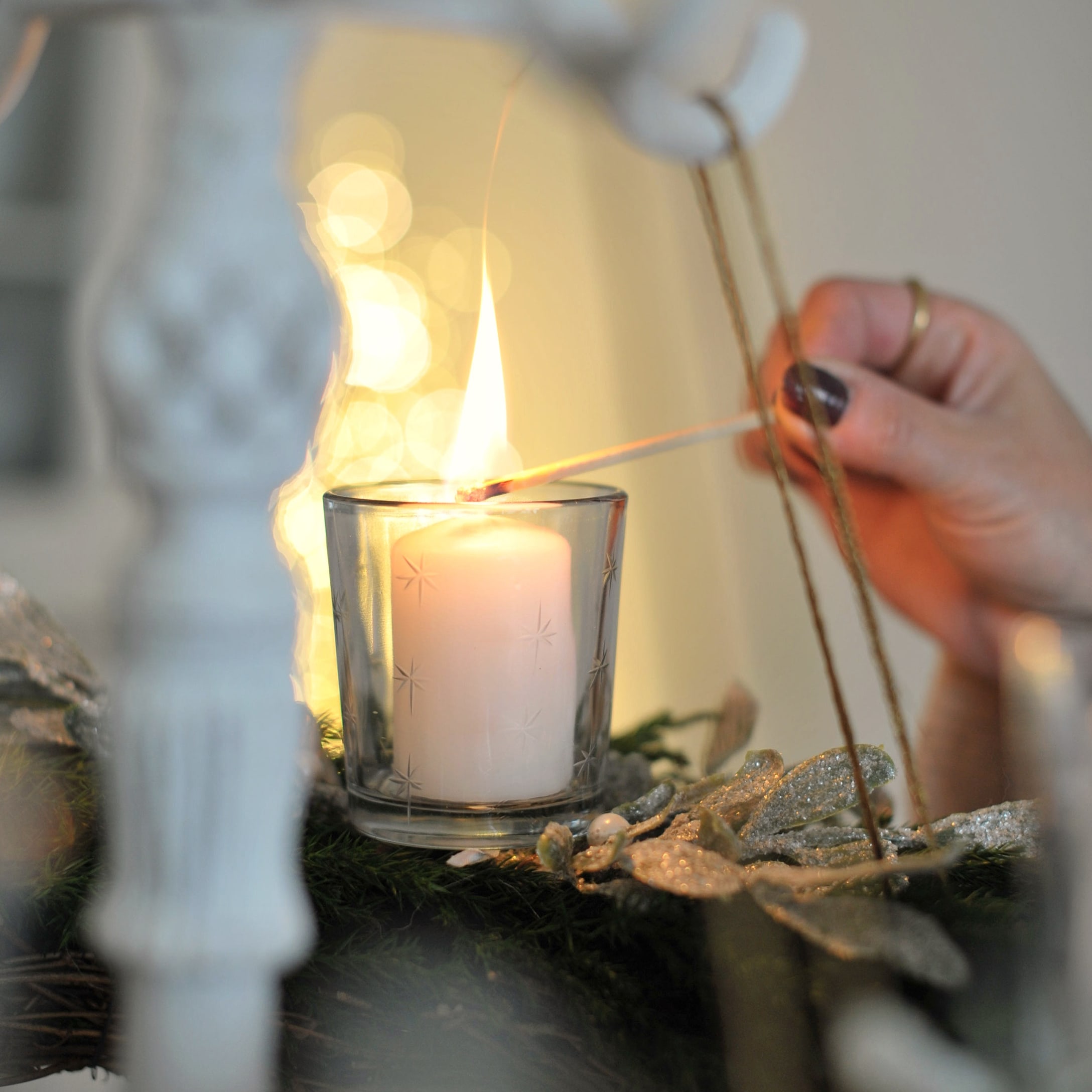 Witte glazen theelichthouder met sterrenpatroon op groene versierde adventskrans