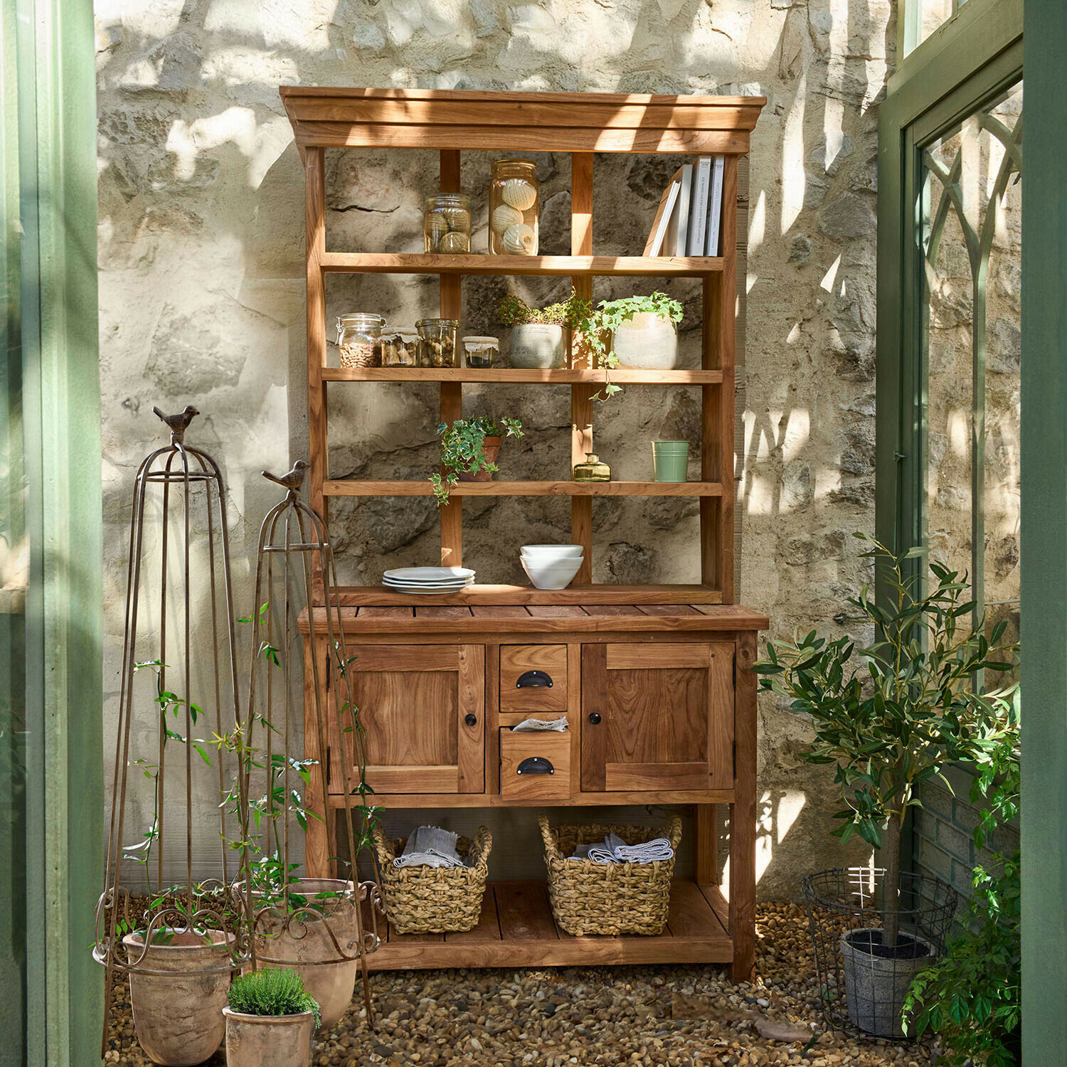 Houten kast in natuurlijke kleur met planken en lades, versierd met planten en serviesgoed