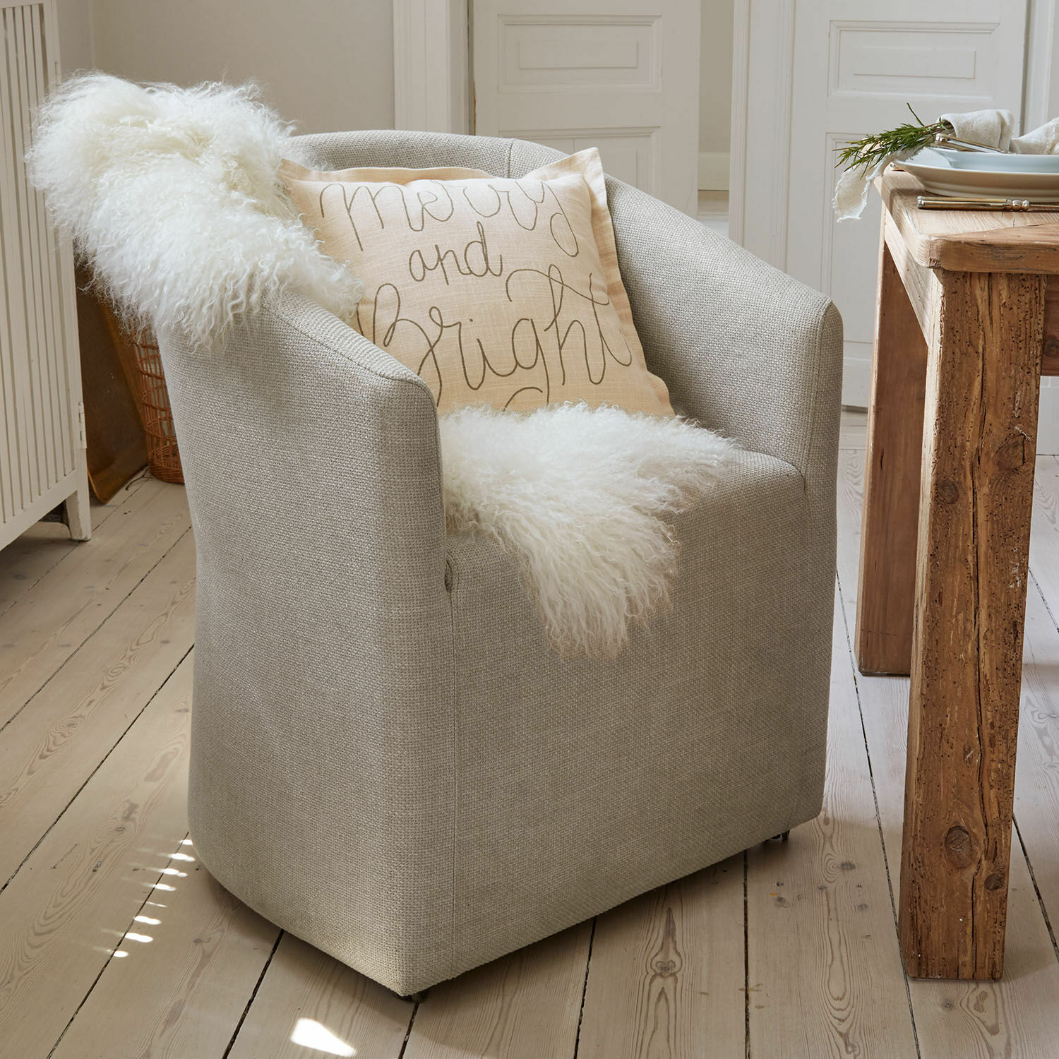 Fauteuil Holmsen Grijze gestoffeerde fauteuil met zachte witte deken en licht sierkussen in Scandinavische stijl