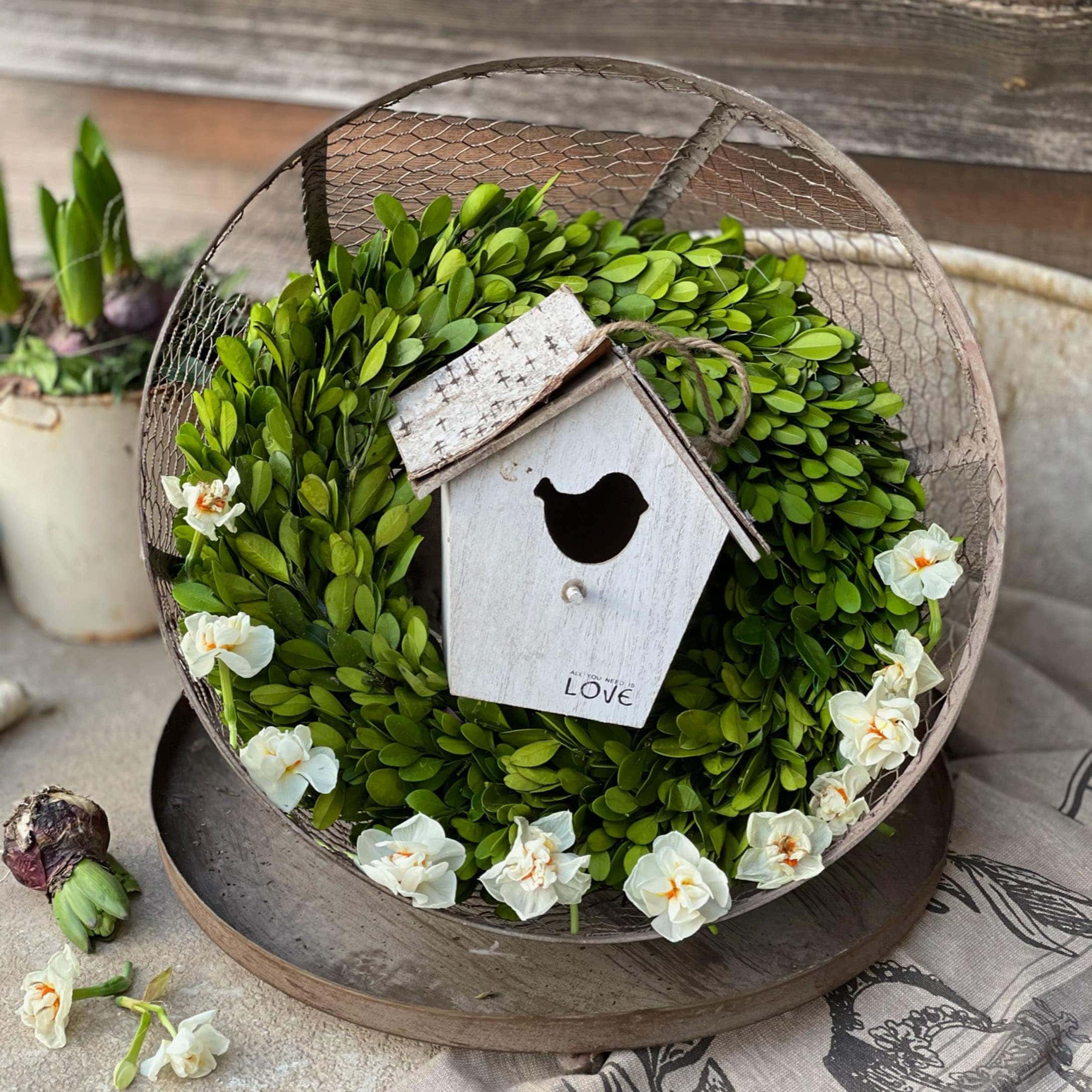 Decoratieve krans van groene bladeren en witte bloemen met houten vogelhuisje op rustieke tafel